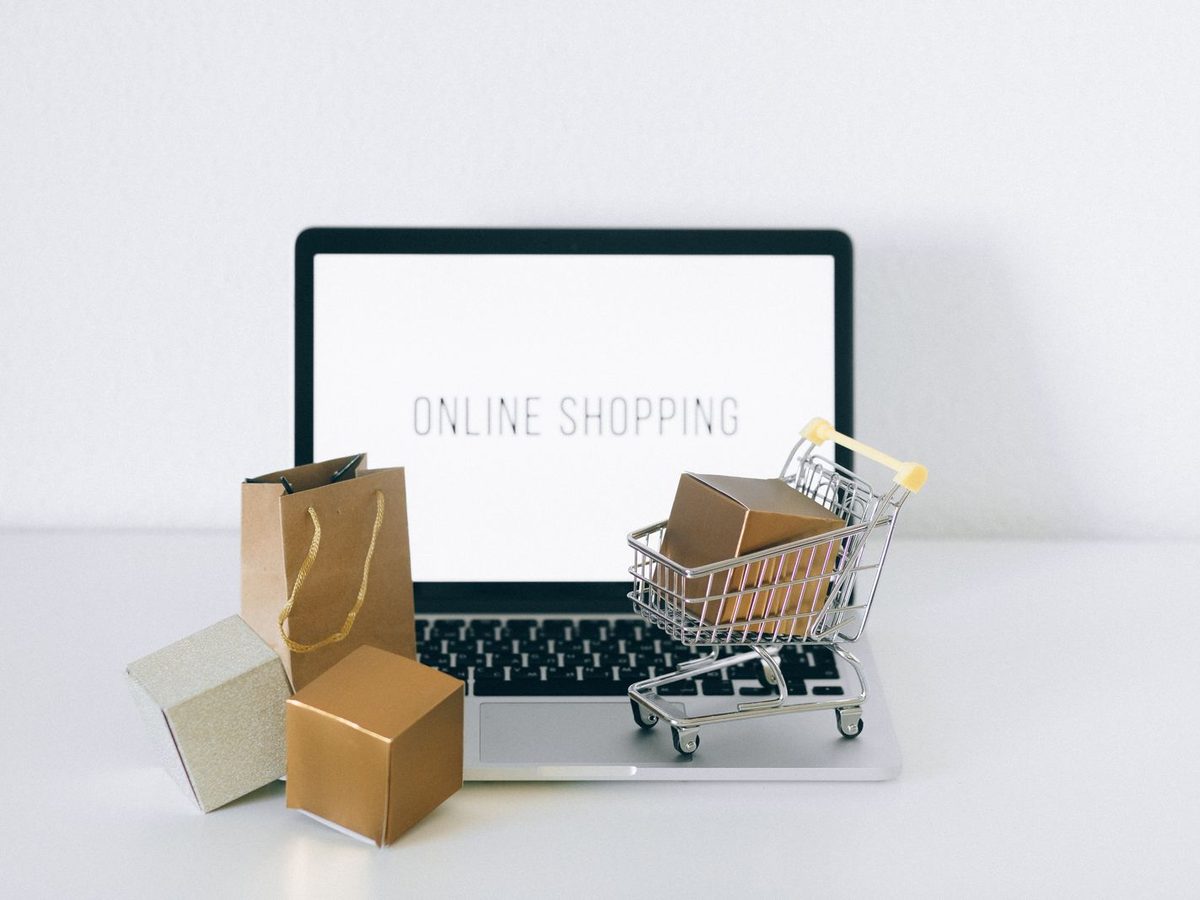 Illustrative photo: a laptop showing an online shop beside a miniature shopping cart and parcels, representing marketplace orders