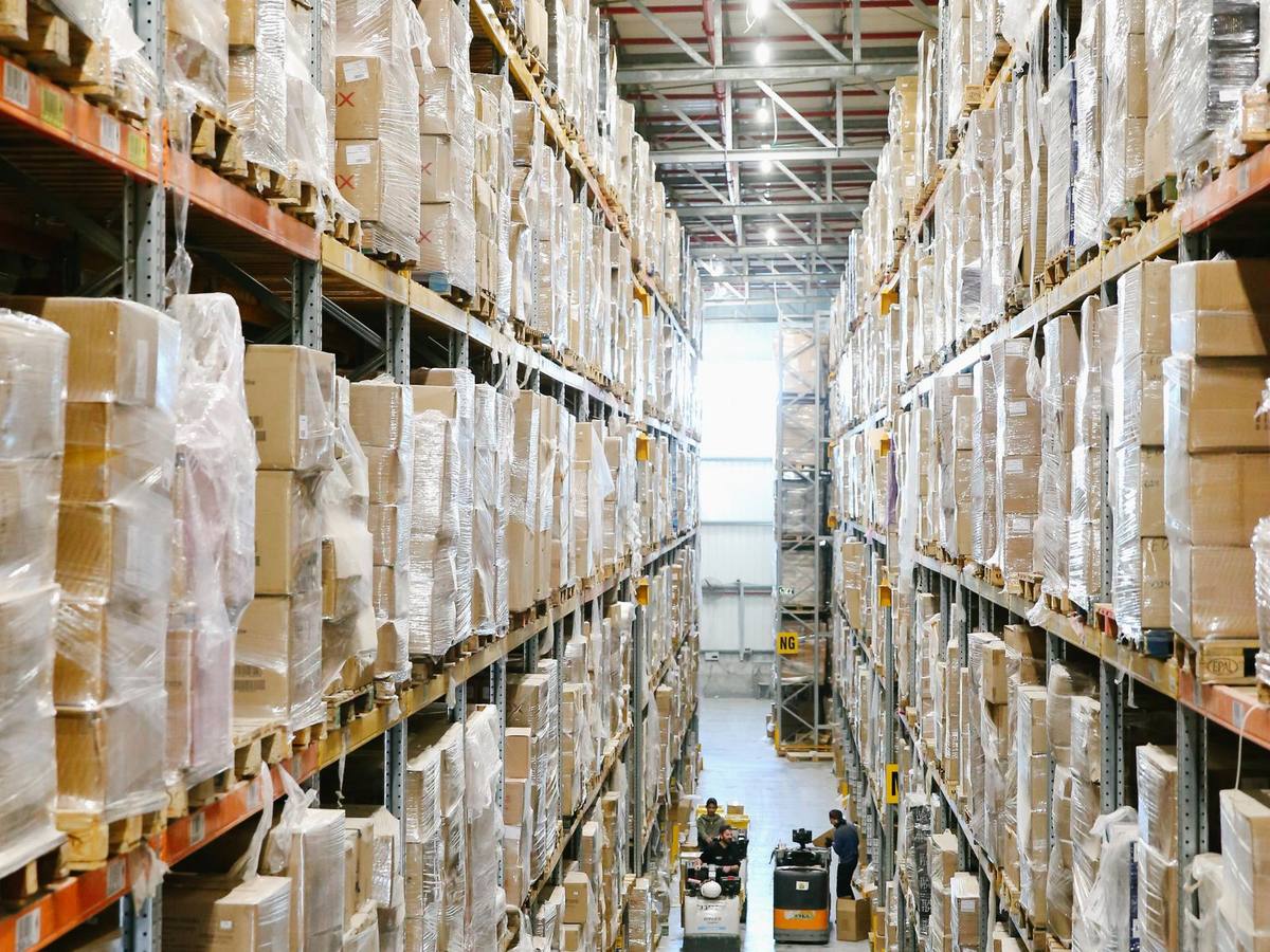 A tall warehouse aisle lined with shelves of shrink-wrapped cartons ready for shipping